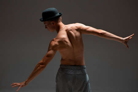 Stylish young guy dancer in hat with naked torso dancing hip-hop in studio. Dance school poster. View from the backの写真素材