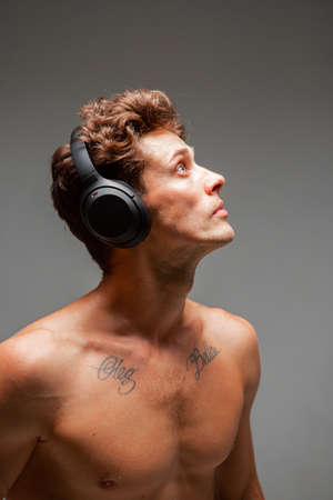 Stylish young man in wireless headphone listening to song with naked shoulders in studio. Music posterの写真素材