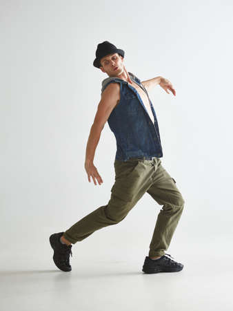 Cool young guy breakdancer in hat dancing hip-hop in studio isolated on white background. Break...