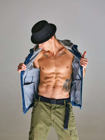 Cool sexy man breakdancer in hat standing in studio isolated on gray background. Dance school poster