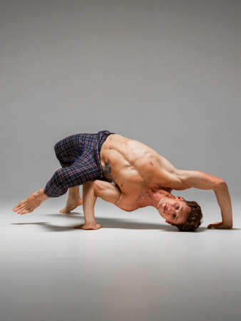 Flexible guy breakdancer with naked torso dancing lower break dance isolated on gray background....