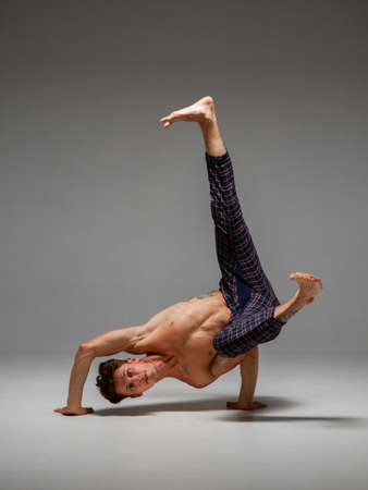 Cool man dancer with naked torso dancing lower break dance isolated on gray background