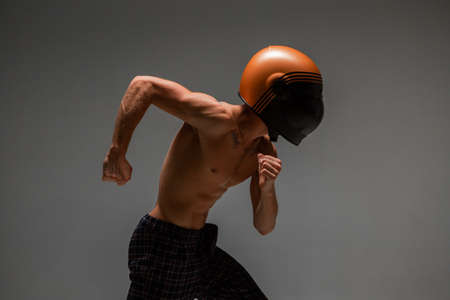 Athletic guy racer in helmet runs on grey background in studio. Kart racing school poster. Body with...