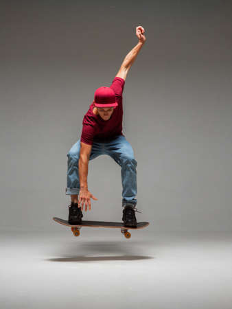 Cool young guy skateboarder levitates on skateboard in studio on grey background. Photography about skateboarding tricksの写真素材