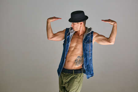 Young guy breakdancer in hat dancing expressive dance in studio isolated on gray background. Body...