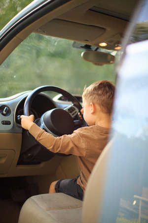 Smiling baby boy small driver holding steering wheel of the car. Back view. Photography for ad or blog about family tripの写真素材