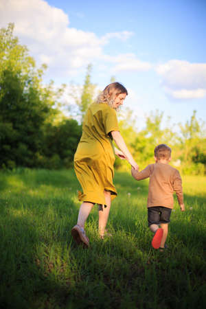 Cute baby boy and mother walking on green lawn. Back view. Summertime photography for ad or blog about motherhoodの写真素材