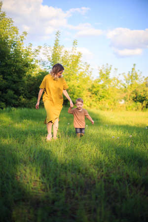 Cute baby boy and mother walking on green lawn. Summertime photography for ad or blog about motherhoodの写真素材