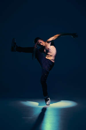Young guy dancer with naked torso dancing in studio in spotlight on black background. Dance school posterの写真素材