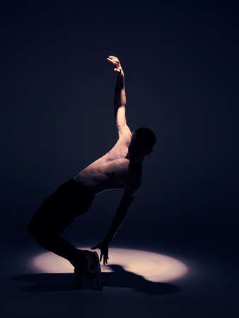 Cool young guy dancer with naked torso dancing in studio in spotlight on black background. Dance school posterの写真素材