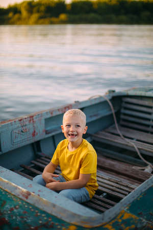 Stylish smiling baby boy sitting on boat on river in summertime, photography for travel blog or family blog or adの写真素材