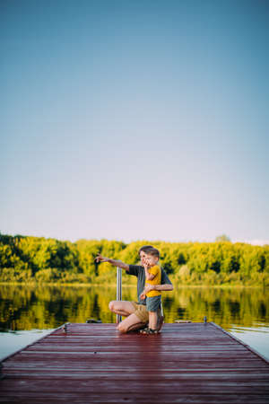 Cool baby boy with mother looking on river standing on pier. Summer photography for blog or ad about family and travelの写真素材