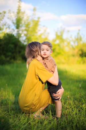 Cute baby boy hugs his mother on green lawn. Summertime photography for ad or blog about motherhoodの写真素材