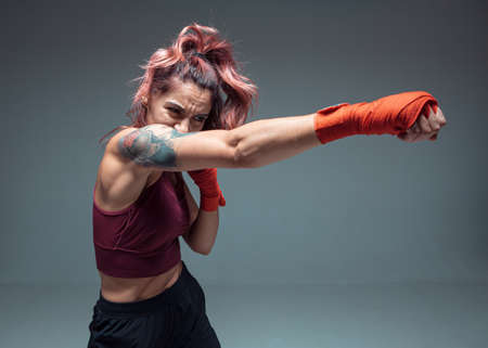 Beautiful female fighter boxing in studio isolated on gray background. Mixed martial arts posterの写真素材