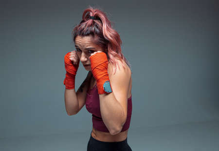 Portrait of female fighter in boxing bandages standing in studio isolated on gray backgroundの写真素材
