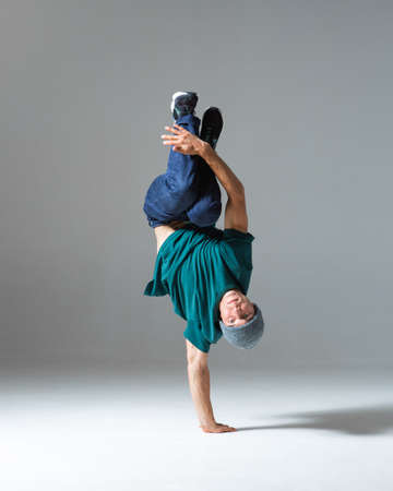 Cool guy breakdancer stands on one hand dancing lower break dance isolated on gray background. Break...