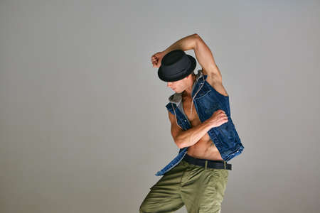 Young guy breakdancer in hat dancing hip-hop in studio isolated on gray background. Dance school...
