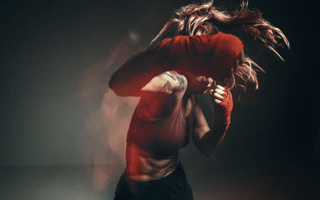 Cool female fighter in boxing bandages trains in studio in neon light. Mixed martial arts poster. Long exposure shotの写真素材