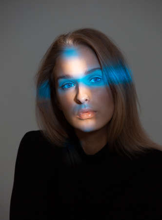 Trendy portrait of beautiful girl with neon light on face isolated on gray background in studio