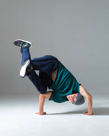 Stylish young guy breakdancer in hat stands on hands dancing hip hop isolated on gray background. Dance school posterの写真素材
