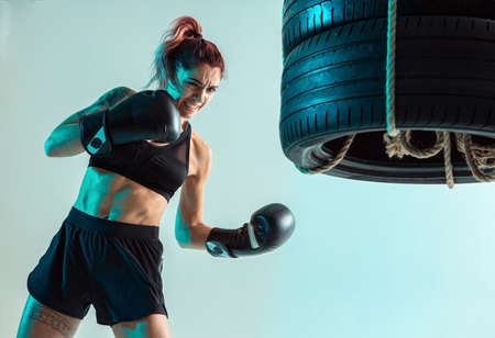 A female fighter in Boxing gloves strikes the tires with her handの写真素材