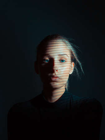 Mysterious portrait of young girl with shadow pattern on her face in black dark studio