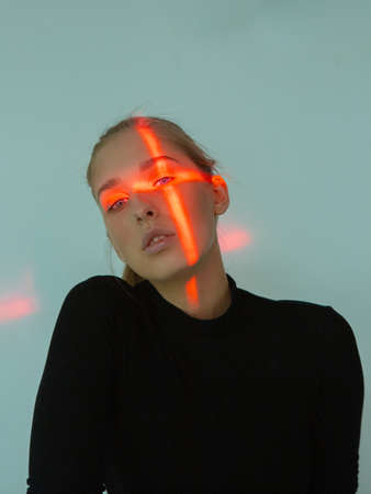 Beautiful young girl with cross shaped red light on her faceの写真素材