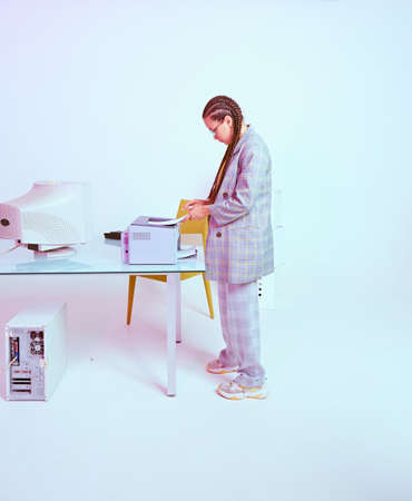 Stylish creative female office worker puts paper in printer in workplace with old computer