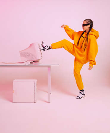 Stylish female office worker in sunglasses and hoodie kicks obsolete computer monitor. Colored Neon...
