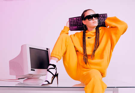 Stylish asian female office worker in sunglasses sitting with obsolete computer and shows tongue....