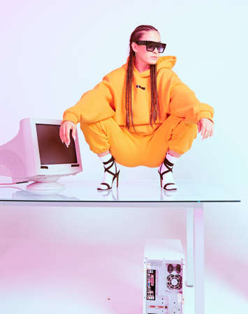 Stylish female office worker with old computer squats on desk. Colored Neon light