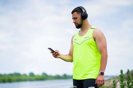 Handsome athletic guy listening to music with headphones on nature background in cloudy weatherの写真素材