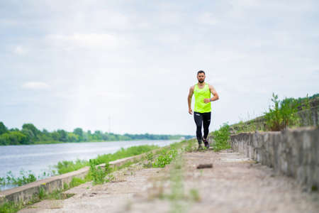 Athletic running guy in stylish sportswear on workout outside in cloudy weather, sport healthy...