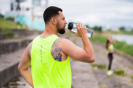 Handsome young athletic guy in stylish sportswear drink water during workout in urban