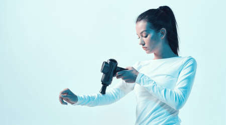 Percussion massager, athletic young brunette female massaging hand in neon studio lightの写真素材