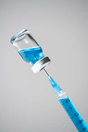 Close up vaccine vial, blue medicine filling up to syringe on gray backdrop.の写真素材
