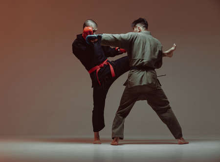 Wrestling of two fighting males in kimono and boxing gloves in red light in studio, martial arts, mixed fight conceptの写真素材