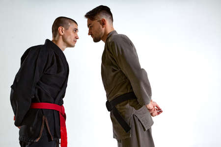 Guys in kimono face to face before karate fight workout on white studio backdrop with copy space, martial arts conceptの写真素材