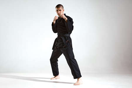 Sportive guy trainer in black kimono fighter posing in karate stance on studio background with copy spaceの写真素材