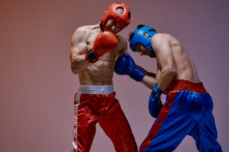 Sparring of two fighting males in helmets and boxing gloves with fit bare torsos during battle, martial artsの写真素材