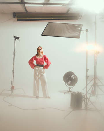 Stylish young pretty female model posing in photo studio with lighting photographic equipmentの写真素材