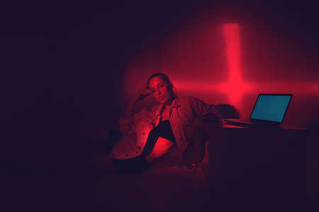 Cool modern girl with laptop in red colored light. Free creativity. Young blogger in home office