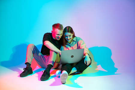 Modern young couple girl and guy working on laptop or shopping online. Colored neon studio lightの写真素材