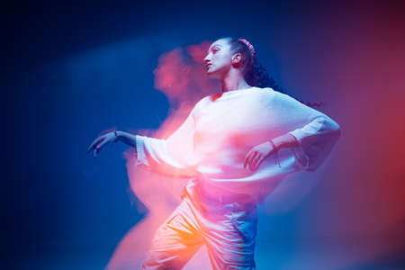 Mixed race young modern girl dancing in colourful neon light. Long exposure. Stylish female moving to rap rhythmの写真素材