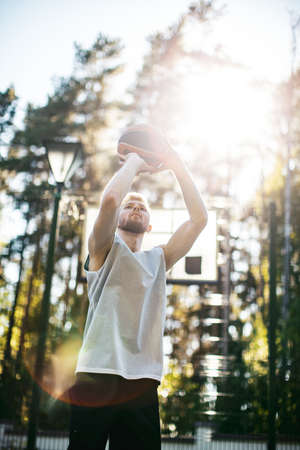 Professional male american basketball player aiming during workout on court outdoors in summer in sunlightの写真素材