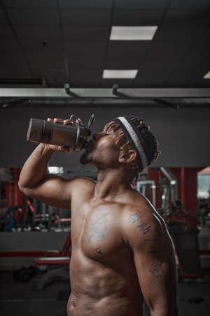 Nutritional supplement. Muscular athletic man drinking protein, energy drink after workout in gymの写真素材