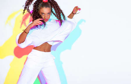 Beautiful dancing mixed race young girl with afro hairs in colourful neon studio light on white background, copy spaceの写真素材