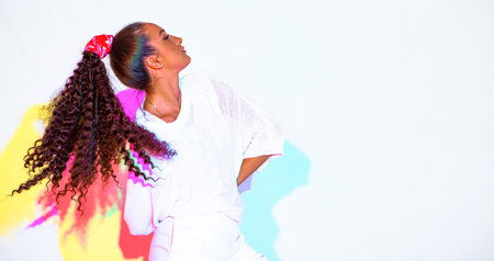 Beautiful mixed race young girl with waving afro hairs in colourful rainbow light on white background with copy spaceの写真素材