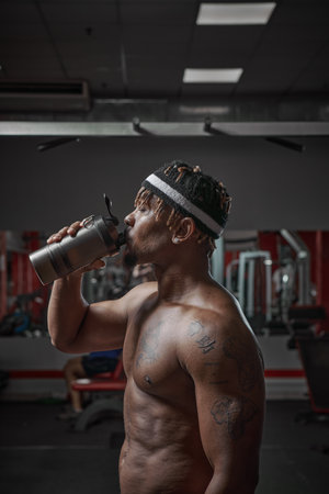 Protein shake after workout and gym training. African american man with naked torso drinking sport drinkの写真素材