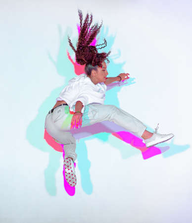 Jumping mixed race young girl jumping in colourful neon studio light. Female dancer performer moving...